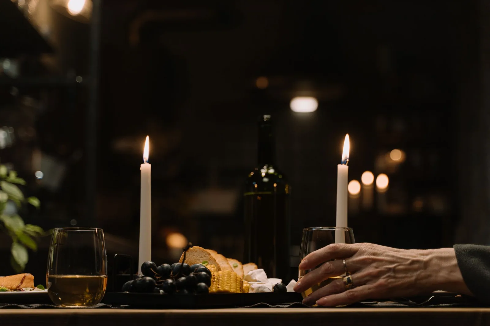 Candles lit on a table at dinner, a glass of wine in hand