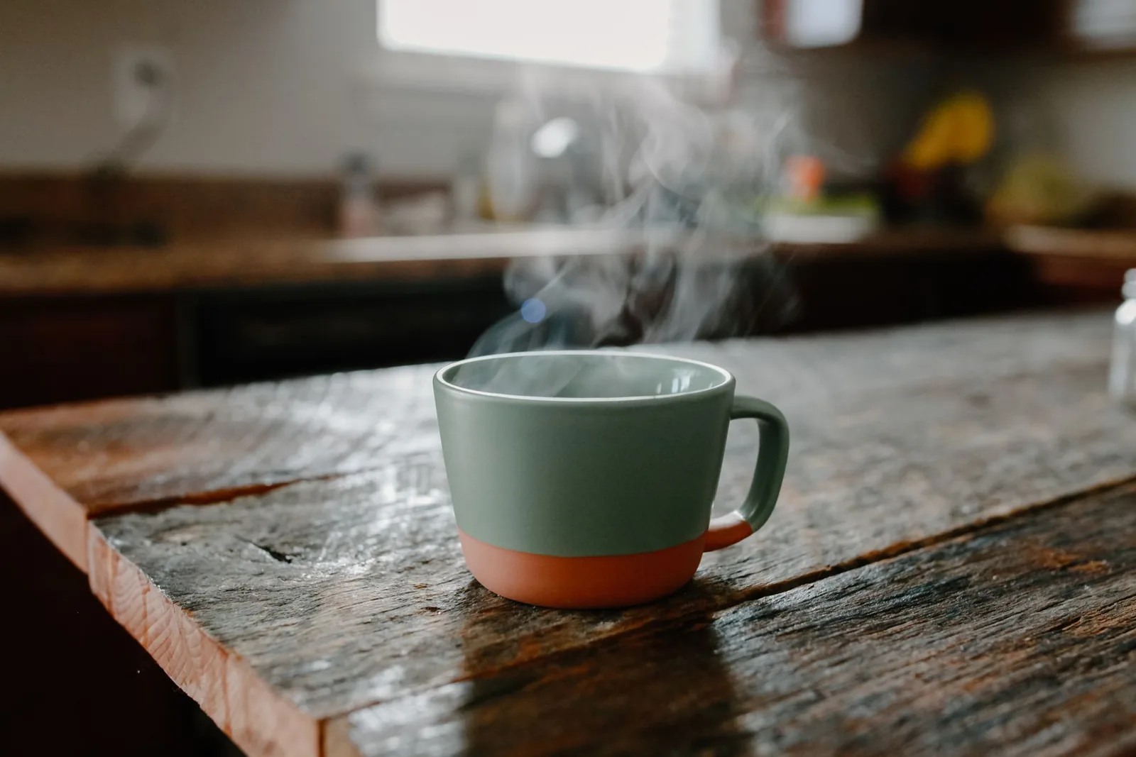 A green mug of something hot, steaming on an old wooden counter